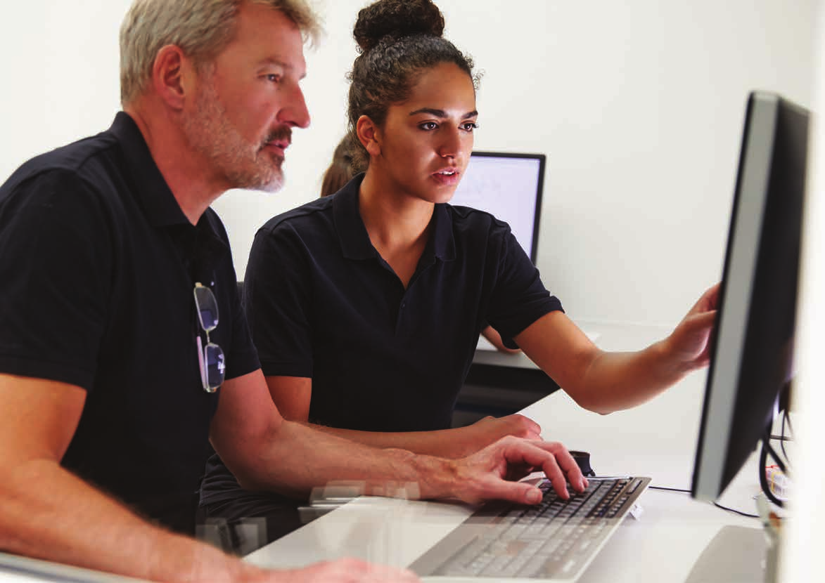 Two people are intently looking at a computer screen while one of them uses the keyboard.