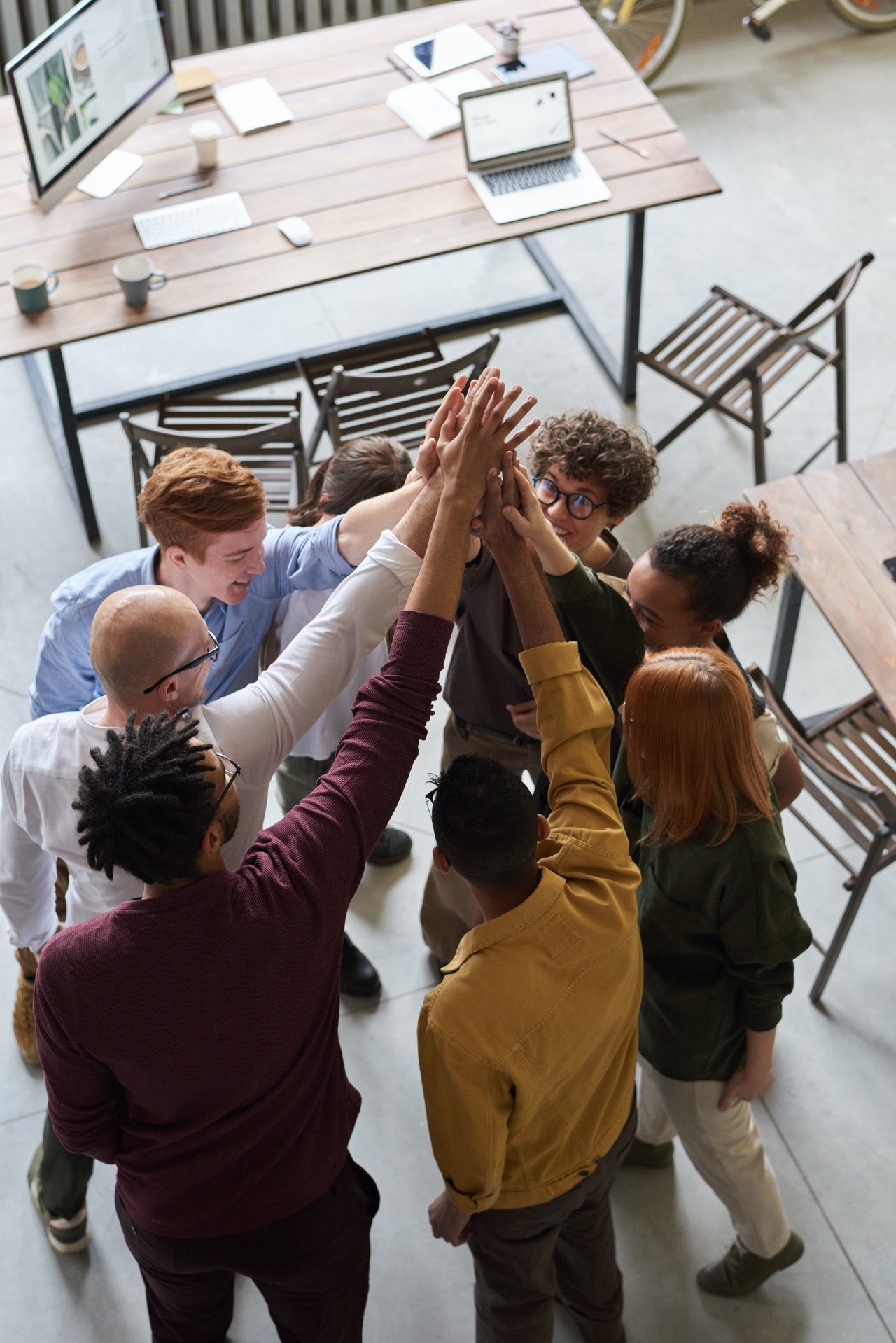 A group of individuals from diverse backgrounds are joyfully participating in a team high-five at a modern office space.